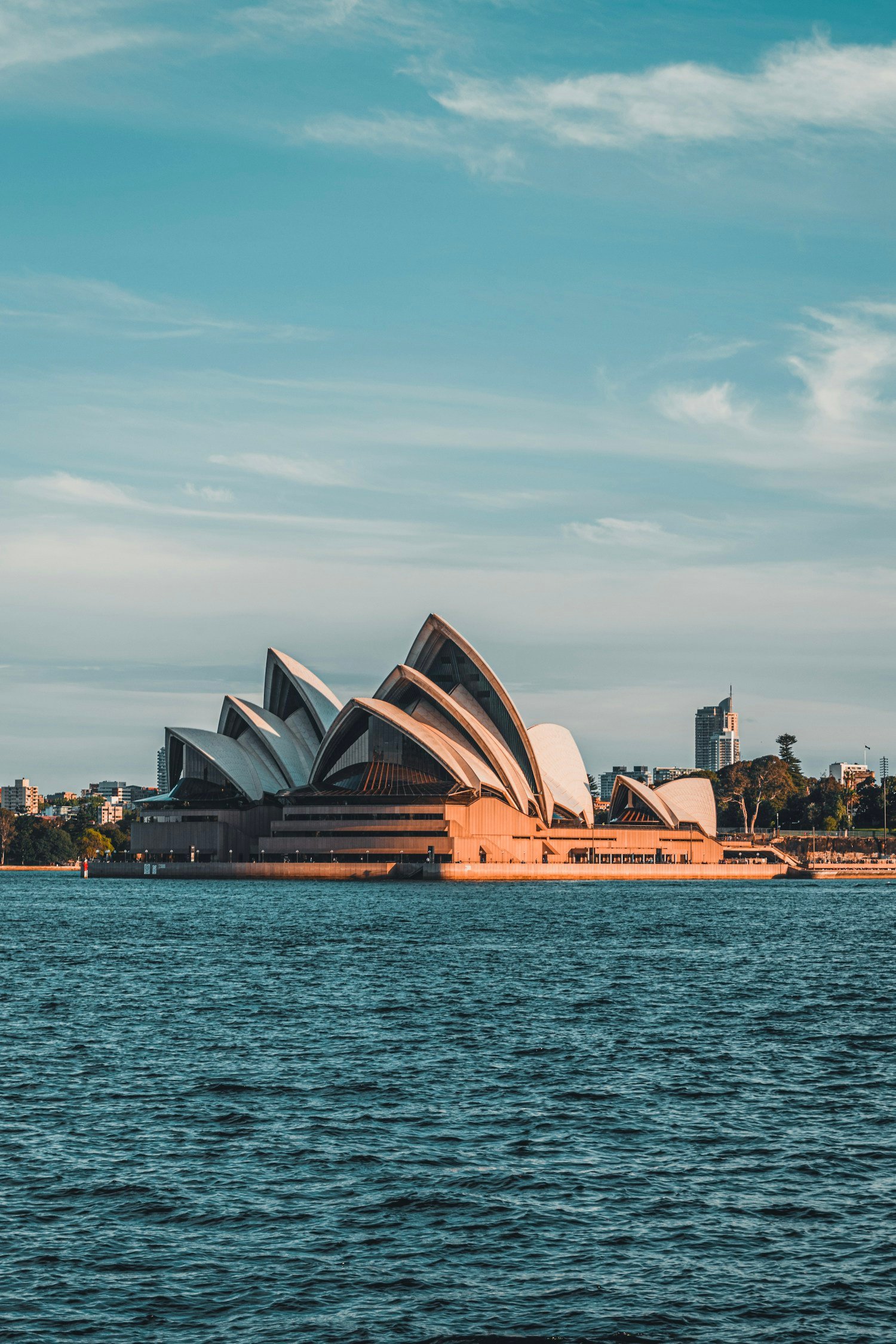 Sydney Opera House in warm evening light across the harbour.